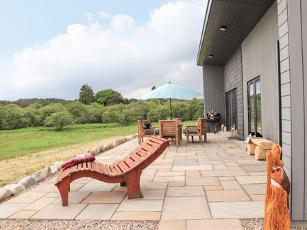An outdoor patio with wooden lounge chair table and chairs with umbrella and a carved wooden bird Pine Marten Dornoch