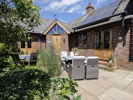An outdoor patio area with tables and chairs next to a brick house with solar panels on the roof at The Old Byre in Woodfalls