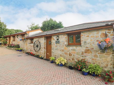 A stone building with wooden doors and windows potted plants on a paved driveway at The Hideaway in St Austell