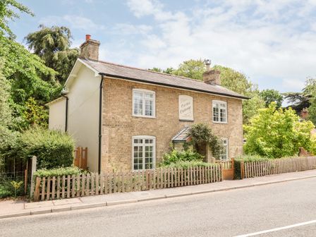 A two story brick house with white framed windows surrounded by greenery and a wooden picket fence at Cavan Cottage in Yoxford