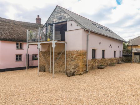 An exterior view of a stone and plaster building with a balcony and a gravel courtyard at Becket's Barn in Northlew