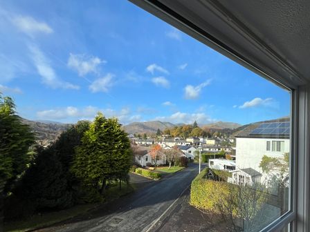 A street view with houses trees and mountains seen through a window at Fairfield View in Ambleside
