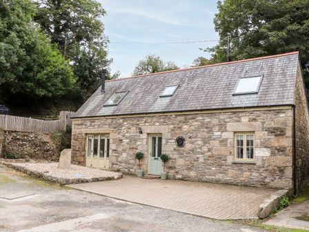 A stone cottage with skylights a green door and windows surrounded by trees at Potters Barn Trevarno near Helston