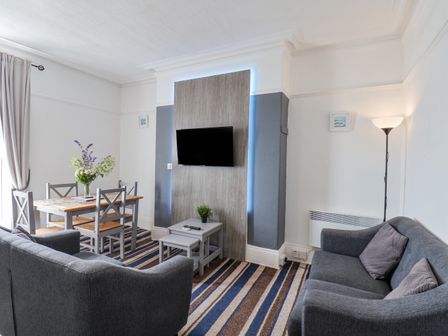 A living room with two gray sofas a dining table with four chairs and a wall-mounted television at Harbour View in Bridlington