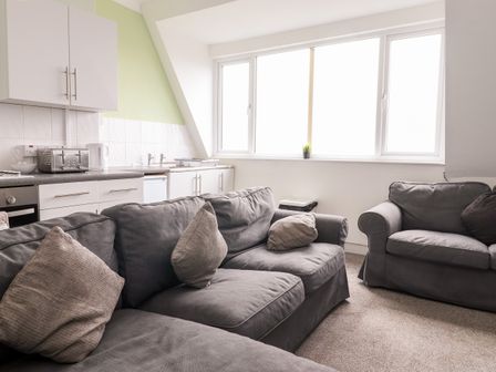 A living area with grey sofas and cushions next to a kitchen space with cabinets toaster kettle and large windows at Bayside in Bridlington