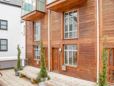 A courtyard with wooden bench and potted plants in front of a wooden building at 5 Harbour Yard Salcombe