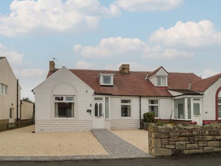 A white single-story house with a red tiled roof and a paved walkway leading to the front door at Gudhjem in Seahouses