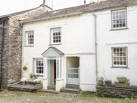 Exterior view of a white cobblestone cottage with green trim and potted plants at Jessamine Cottage in Hawkshead