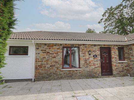 The exterior of a stone and white house with three windows a door and a paved patio at Sea View in St Clears