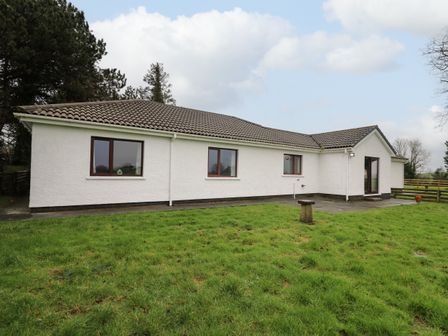 A white single-story house with a tiled roof and three windows overlooking a grassy yard at The Oaks in St Clears