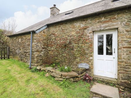 Stone exterior wall with white door and small garden area with plants and sign outside a cottage at The Bake House in Bettws