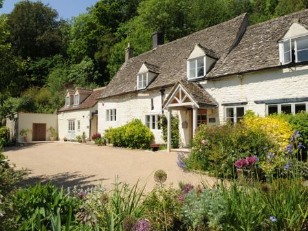 A stone cottage with a gravel driveway and garden in front at Spring Cottage in Stroud