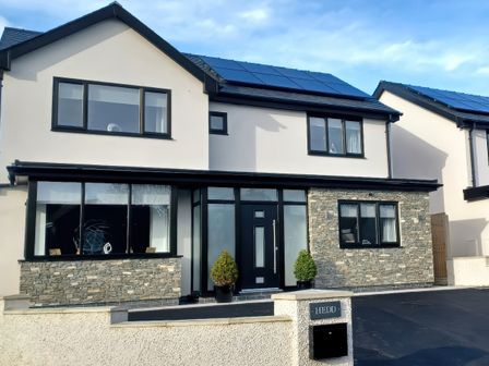 A modern two-story house with stone and white exterior walls solar panels on the roof and a black front door at Hedd in Amlwch