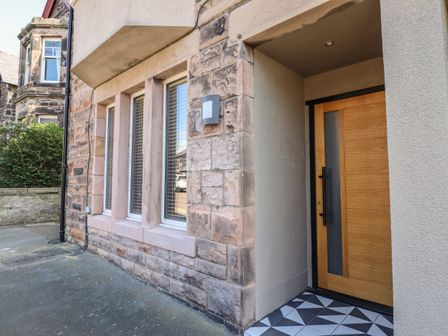 An exterior view of a stone building with three windows and a wooden front door with geometric tiled flooring at Glencoe House in Wooler
