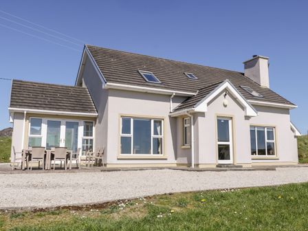 A two-story house with several windows and a patio table with chairs outside at Inverbeg Cottage 1 in Downings