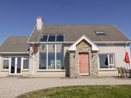 A house with a tiled roof a stone entrance with a red door large windows and an outdoor seating area with an umbrella at Inverbeg Cottage 2 in Dundooan Lower near Downings