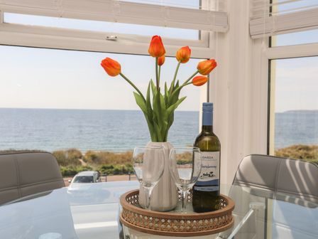 A glass table with a vase of orange tulips wine bottle and two wine glasses by windows overlooking the sea at Tir a Mor in Pwllheli
