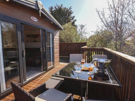 A deck with a glass table set with drinks and snacks outside a wooden cabin at Tulip Lodge in Runswick Bay near Staithes