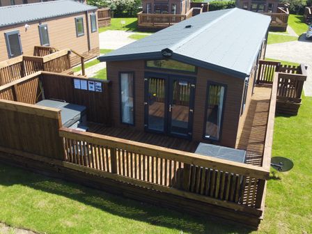A wooden cabin with a fenced deck and outdoor seating at Honeysuckle Lodge in Runswick Bay near Staithes