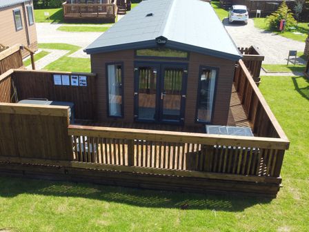 A wooden cabin with a fenced porch and patio furniture in a grassy area