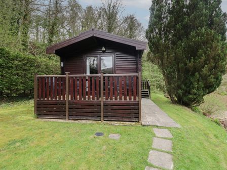 A wooden cabin with a fenced porch surrounded by trees and grass at Canadian Cabin 37 in Keswick