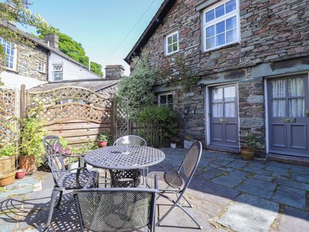 An outdoor patio with a round metal table and four chairs in front of a stone house at Bakers Yard Cottage in Grasmere