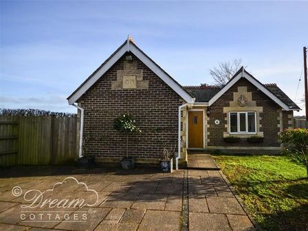 A brick cottage with a paved driveway a wooden door and a small lawn at Frome Lodge House in Frome Whitfield