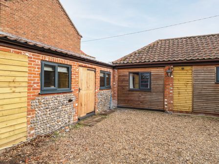 The exterior courtyard of a building with gravel ground brick and wooden walls and windows at Squirrel Lodge in North Walsham