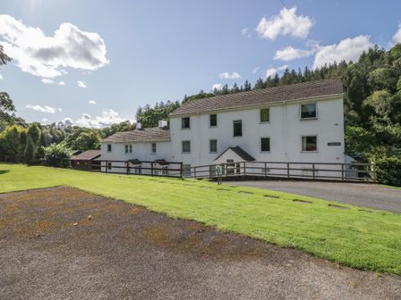 A white multi-story building with a sloped roof surrounded by grass and trees at Garden Cottage No 1 in Keswick