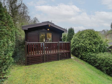 A wooden cabin with a small porch and railing surrounded by greenery at Canadian Cabin No 38 in Keswick