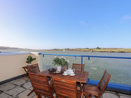 An outdoor terrace with wooden chairs and table overlooking a river at Dornberg in Y Felinheli