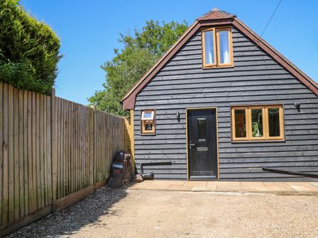 A black wooden house with brown framed windows and door next to a wooden fence at Foxes Earth in Nomansland