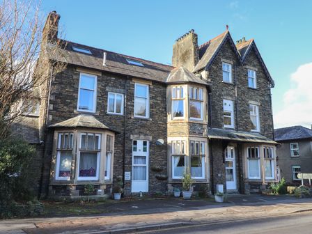 A stone building with multiple windows and doors alongside a paved road at Wansfell Loft in Ambleside