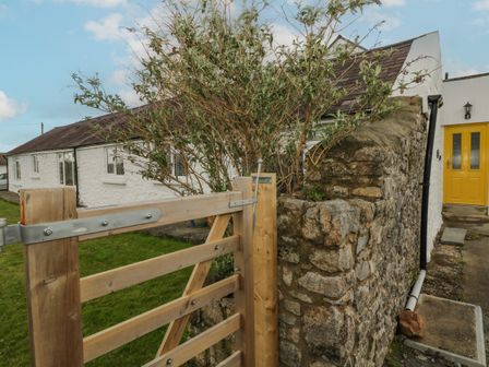 A wooden gate with a stone wall and a white house with a yellow door in the background at Primrose Cottage in Manorbier