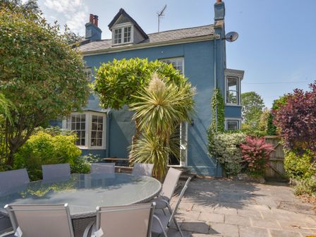 A patio with a glass table and chairs surrounded by trees and bushes at Braeside in Lyme Regis