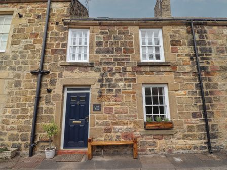 Stone cottage exterior with blue door bench and window flower box at Lark Rise in Alnmouth