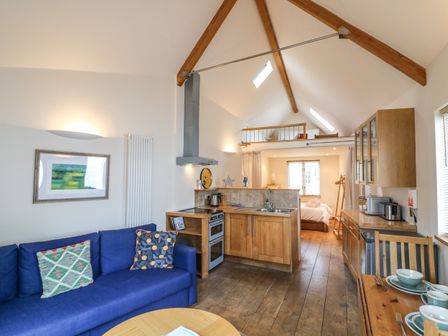 An open living space with a blue sofa kitchen area and dining table leading to a bedroom at The Loft Cottage in Totnes