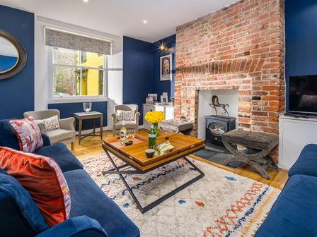 A living room with blue walls a brick fireplace two sofas armchairs and a wooden coffee table at The Indigo House in Berwick-Upon-Tweed