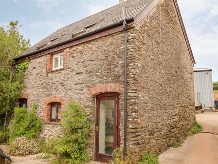 Exterior view of a stone barn with a glass door and small windows surrounded by plants at Higher Norton Barn in East Allington Devon