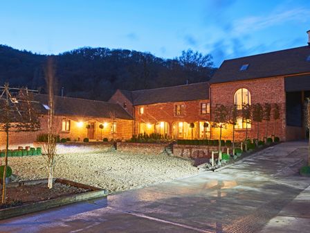 An outdoor courtyard area with brick buildings and lit windows at dusk at The Millhouse in Ledbury near Welland