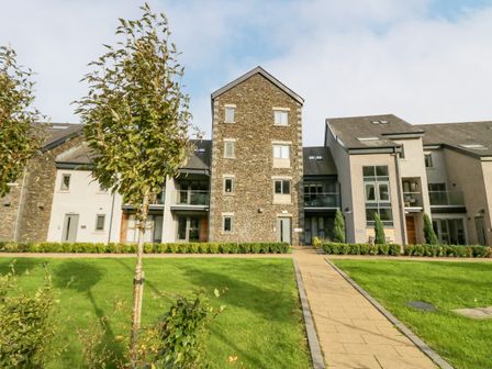 A modern apartment building with a stone facade and pathways surrounded by green grass and trees at Watch Tree Apartment in Backbarrow