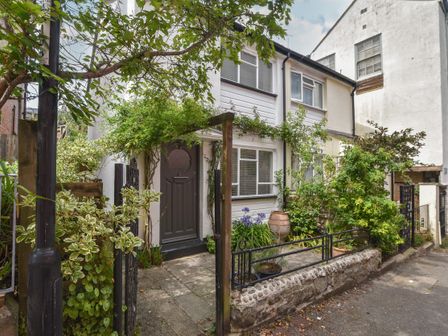 An exterior view of a two-story house with a gray front door and white walls surrounded by plants and shrubs at Whiteleaf Cottage in Lyme Regis