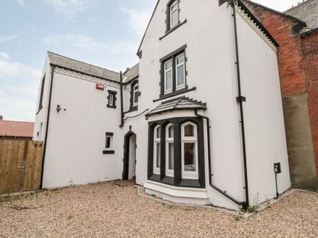 An exterior view of a white house with black trim around windows and door with a gravel yard at Castle Manor in Scarborough