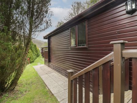 An exterior side view of a brown wooden cabin with a small pathway and green grass at Canadian Cabin No 39 in Keswick