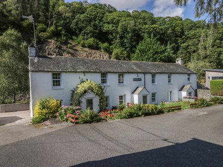 A white cottage with a garden and greenery in front with trees behind at Riverside Cottage No 4 in Keswick