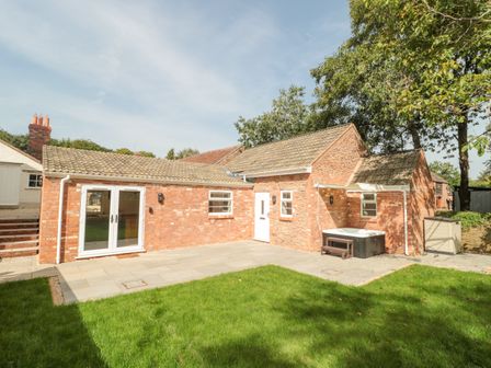 A brick house with a tiled roof a small lawn and a patio area with a hot tub at The Nest in North Petherton