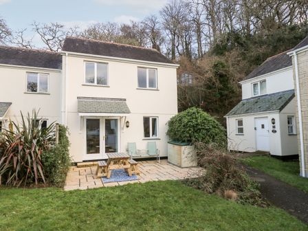 A backyard patio with a picnic table and chairs outside a two story house at Chellowdene Cottage in Falmouth