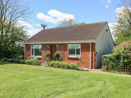 A bungalow with red brick front and tiled roof surrounded by grass and trees at Lavender Lodge in Haverfordwest