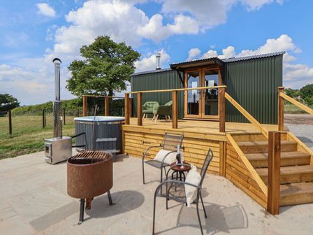 An outdoor patio with chairs a fire pit hot tub and a wooden deck at The Coop in Aston near Woore