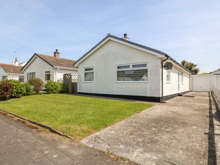 A single story white house with a driveway garage and lawn at Jacuma in Rhosneigr